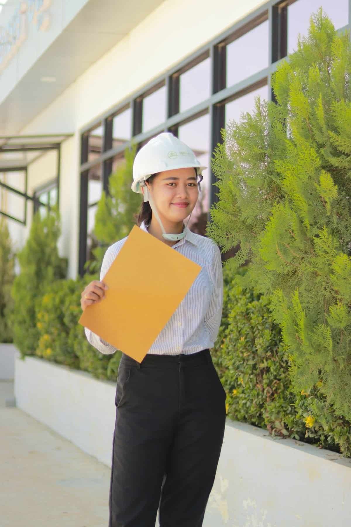 Asian woman wearing a hard hat and holding a clipboard on a worksite, representing WSH Act safety inspection duties
