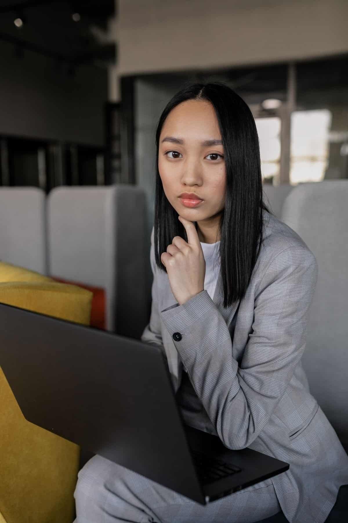 Serious-looking Asian woman with a laptop in an office setting, representing workplace harassment and grievance handling processes